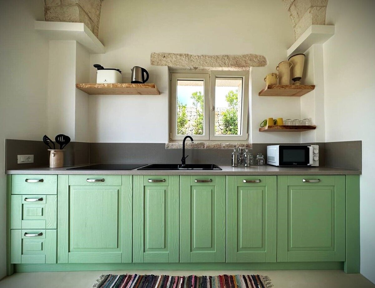 A kitchen with green cabinets, a sink, a window, and a microwave.