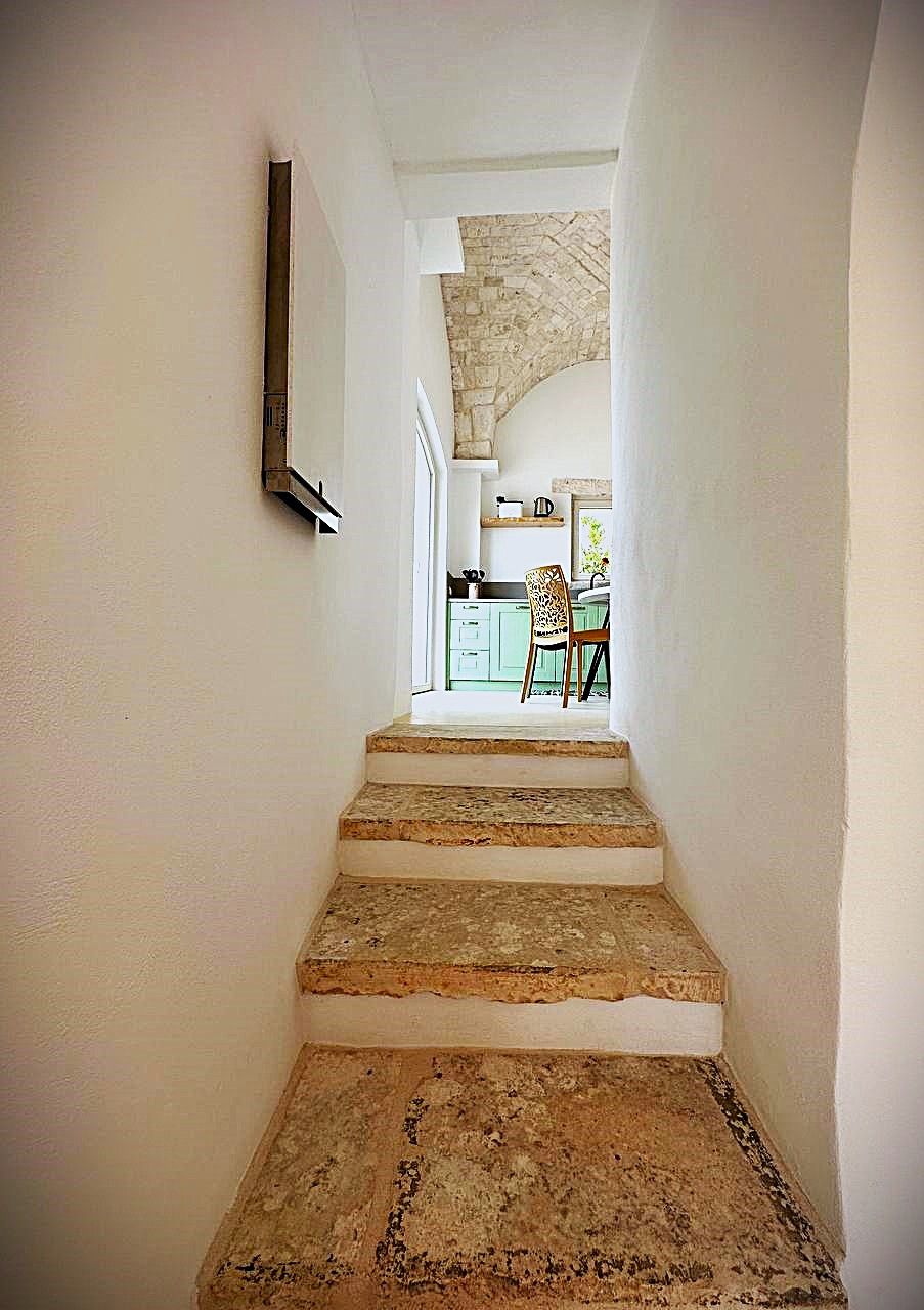 A staircase leading to a kitchen area with green cabinets and a chair.
