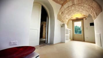 A hallway with a stone archway, a red basin, and a door leading to a room with a view.