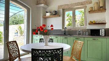 A kitchen with green cabinets, a white dining table, and chairs. There is a window with a view of greenery outside.