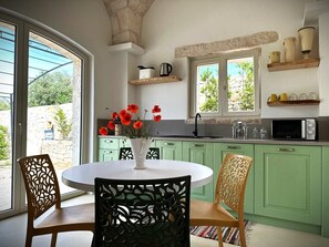 A kitchen with green cabinets, a white dining table, and chairs. There is a window with a view of greenery outside. - Charming Trulli & Lamie in Locorotondo • 2 BR • 2 BA (1 Ensuite) • Patio (Puglia)