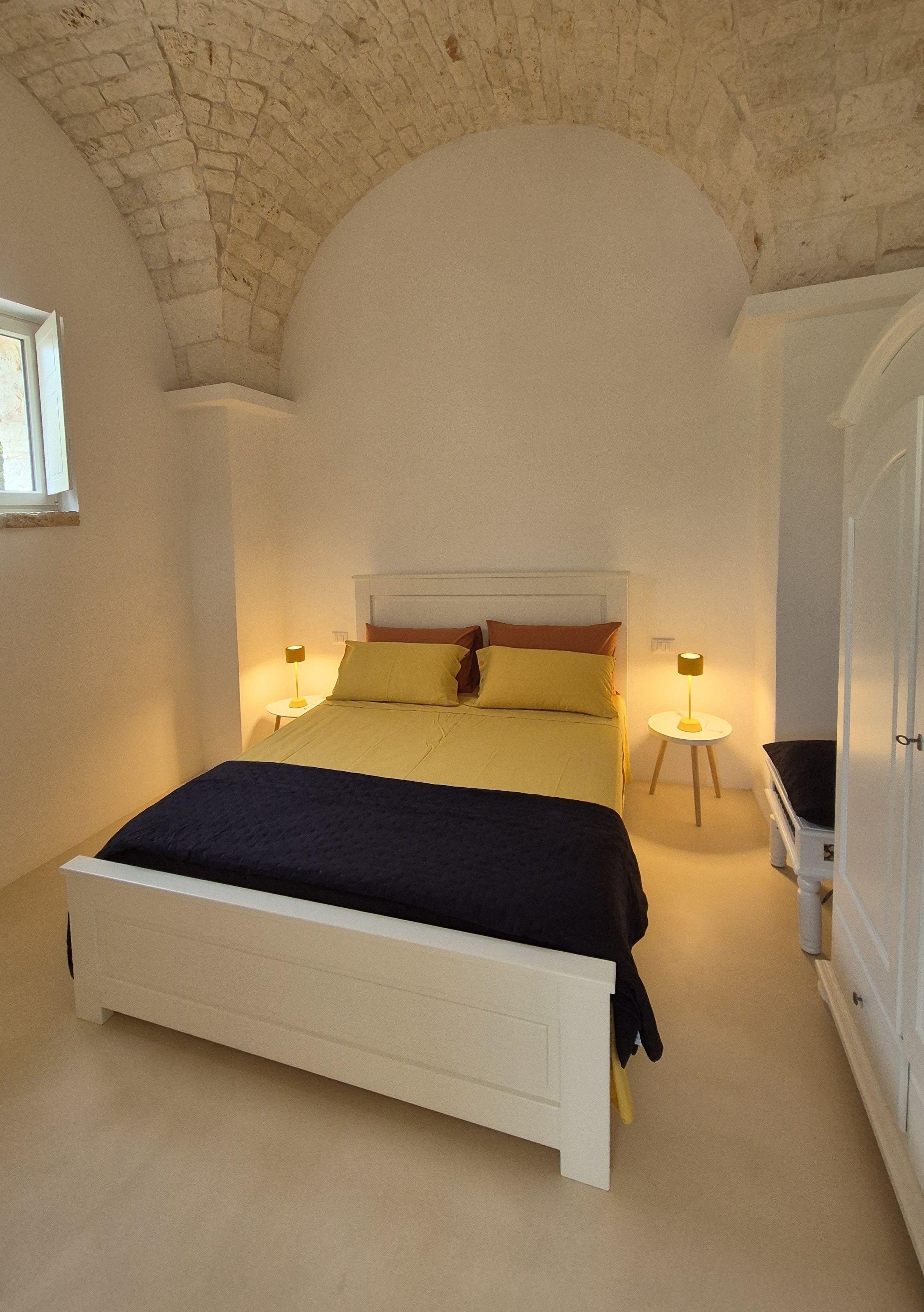 A bedroom with a large bed, two bedside tables with lamps, a wardrobe, and a window.