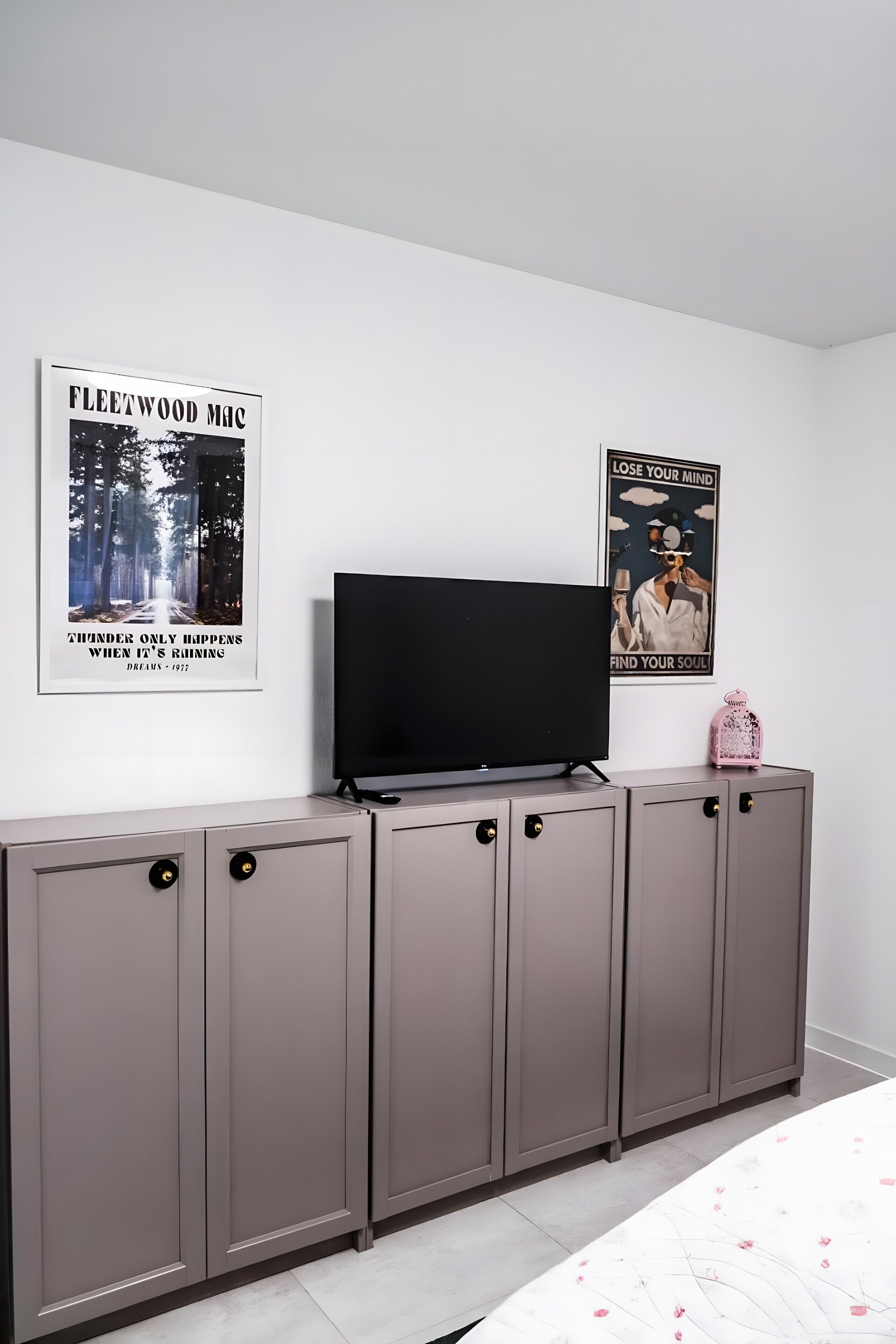 A room with a TV on a grey cabinet, two posters on the wall, and a pink decorative item.