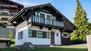 Ein traditionelles Chaletgebäude mit Balkon, Steinunterbau und einem Schild, das angibt, dass es Teil eines Hotels ist.