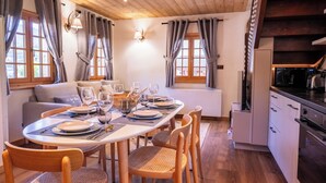 Ein Essbereich mit einem runden Tisch, gedeckt für vier Personen, Holzstühlen, einer Couch und einer Küchenzeile mit Kühlschrank und Herd.