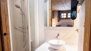 Ein modernes Badezimmer mit einer in Glas eingefassten Dusche, einem weißen Waschbecken und einem hölzernen Waschtisch.