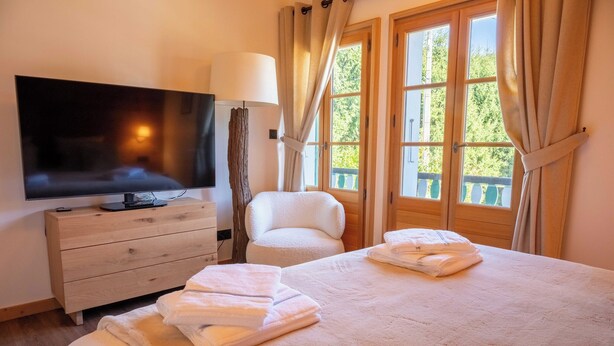 Ein Hotelzimmer mit einem Bett, einem Fernseher, einer hölzernen Kommode und einem Fenster mit Vorhängen.