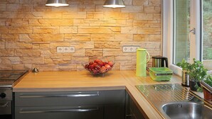 Een keuken met een stenen muur, twee hanglampen, een fruitschaal, een waterkoker, een spoelbak en een raam.