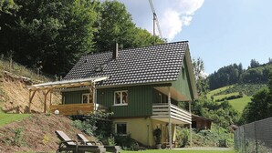 Een huis met twee verdiepingen, een schuin dak, een balkon en een klein terras.