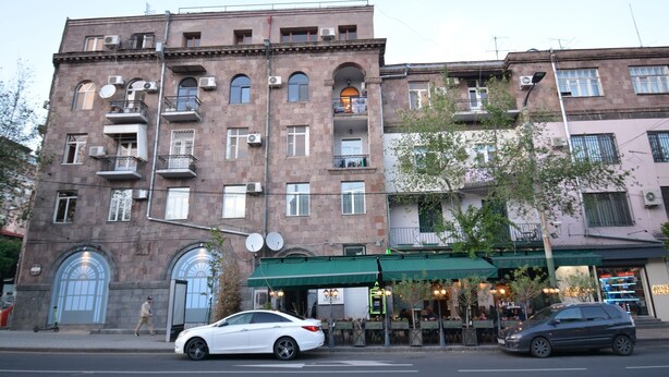A multi-story building with balconies, a green awning, and a storefront with outdoor seating.