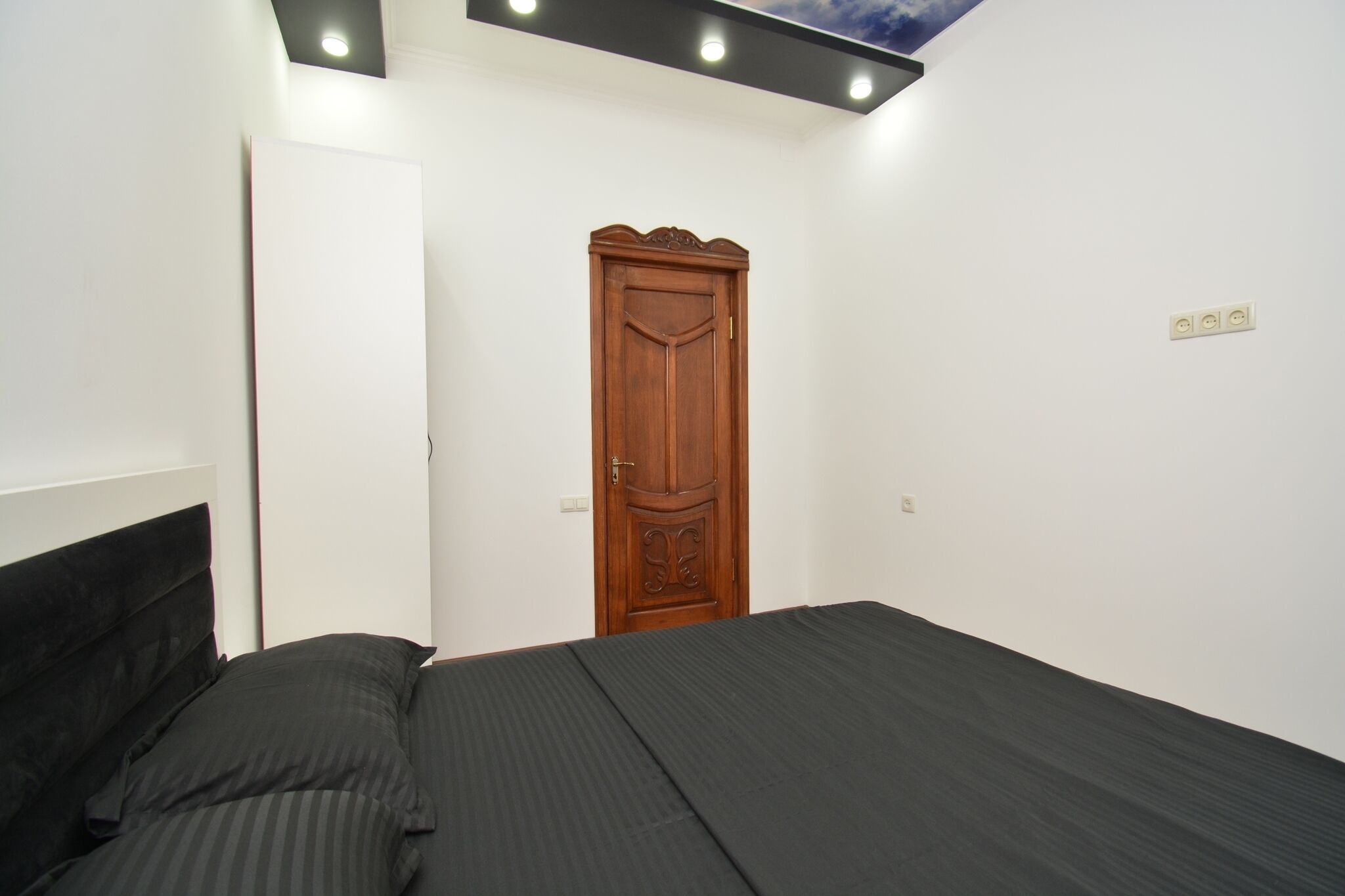 Quarto com cama, guarda-roupa de madeira e luminária no teto.