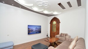 A modern living room with a wooden floor, a large sofa, a small table, and a television mounted on the wall.