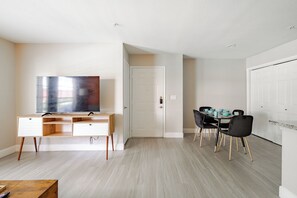 A modern living room with a flat-screen TV, a wooden desk, a dining table with chairs, and a white door. - Coral 1Bed 1Bath facing NRG also Free Parking & Pool (Houston)