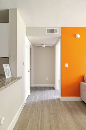 A hallway with a kitchen on one side, a living area with an orange accent wall, and a door leading to another room. - Coral 1Bed 1Bath facing NRG also Free Parking & Pool (Houston)