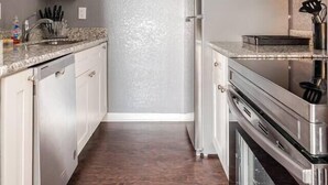 A narrow kitchen with white cabinets, a stainless steel refrigerator, and a microwave.