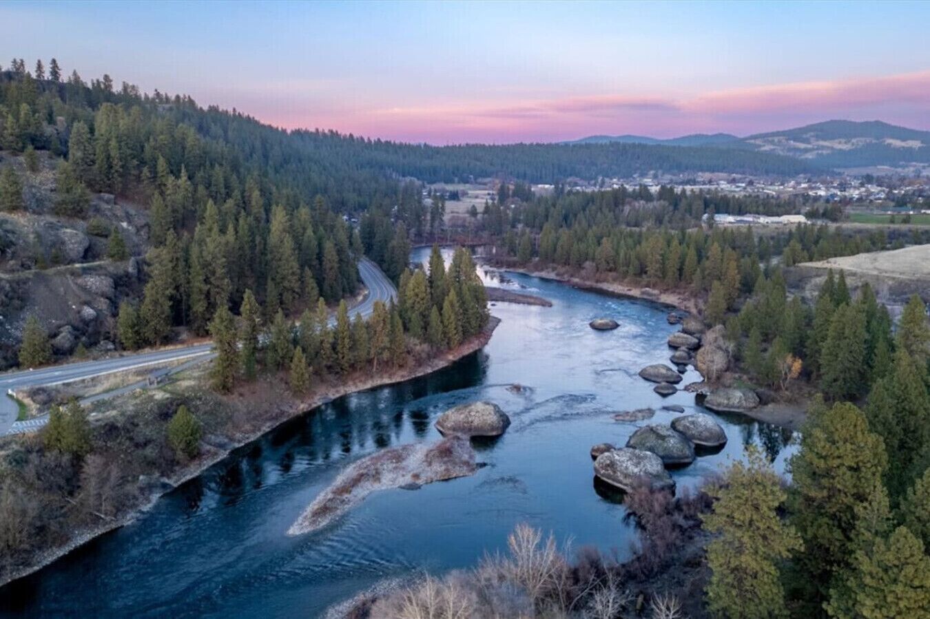 A river winding through a forested valley with a road on the left and a town in the distance.