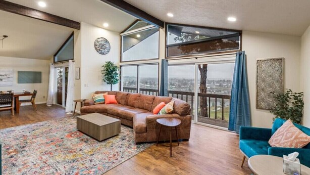 A spacious living room with a large window, a brown leather sofa, a blue sofa, and a wooden coffee table. - River House with Panoramic Views (Spokane)