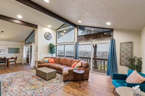 A spacious living room with a large window, a brown leather sofa, a blue sofa, and a wooden coffee table. - River House with Panoramic Views (Spokane)