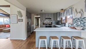 A modern kitchen with grey cabinets, a central island with stools, a microwave, and a stainless steel refrigerator. - River House with Panoramic Views (Spokane)