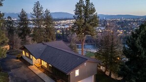A two-story house with a garage, surrounded by trees and a view of a cityscape at dusk. - River House with Panoramic Views (Spokane)