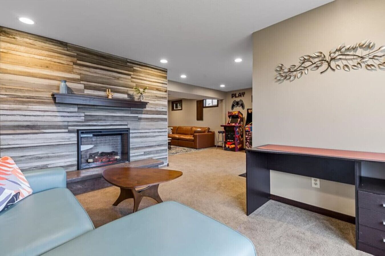 A modern living room with a fireplace, a gaming area, and a desk.