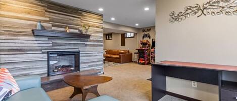 A modern living room with a fireplace, a gaming area, and a desk.