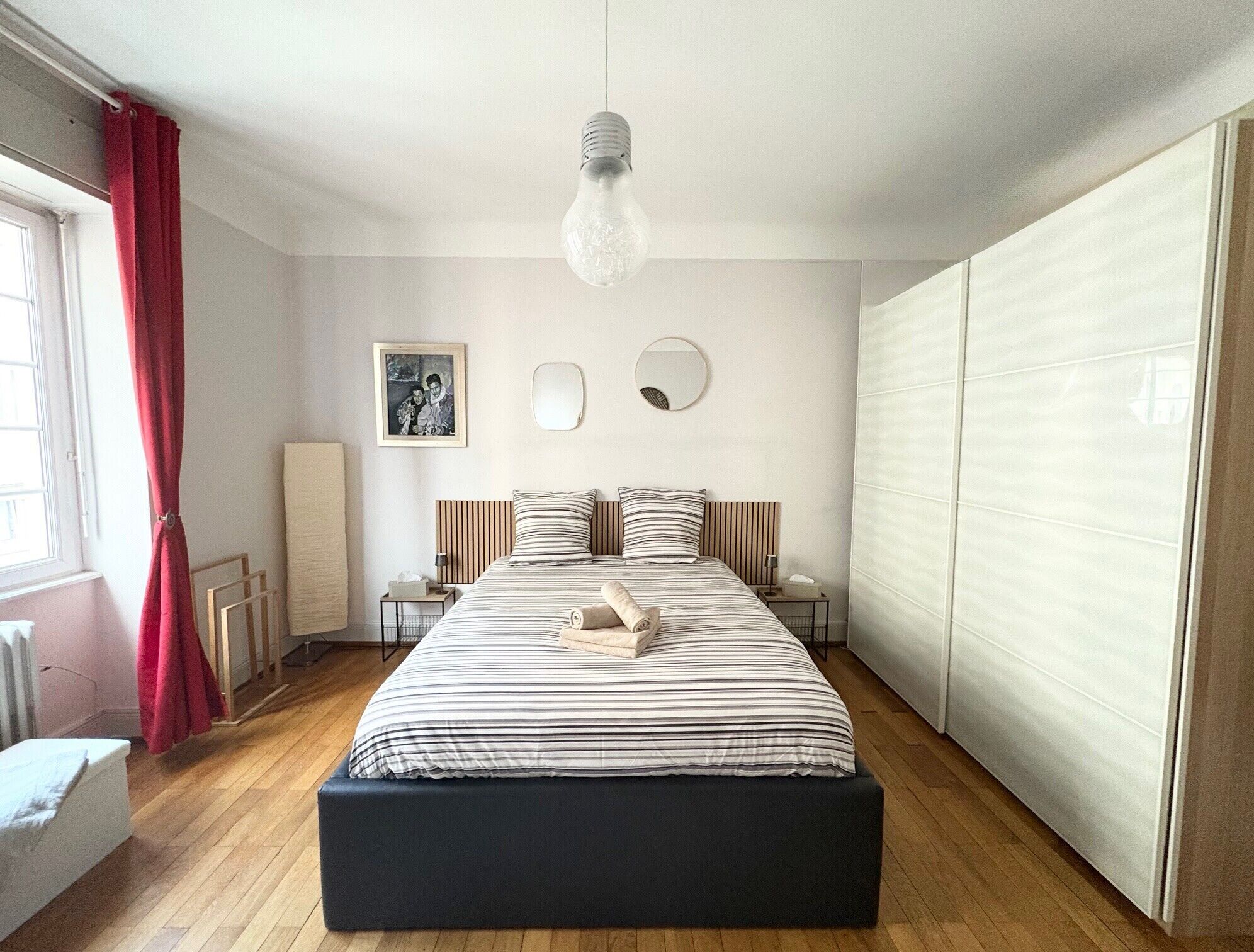 Une chambre à coucher comprenant un lit, des tables de chevet, un luminaire suspendu, un miroir et une armoire.