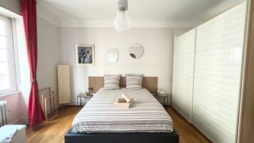 Une chambre à coucher comprenant un lit, des tables de chevet, un luminaire suspendu, un miroir et une armoire.