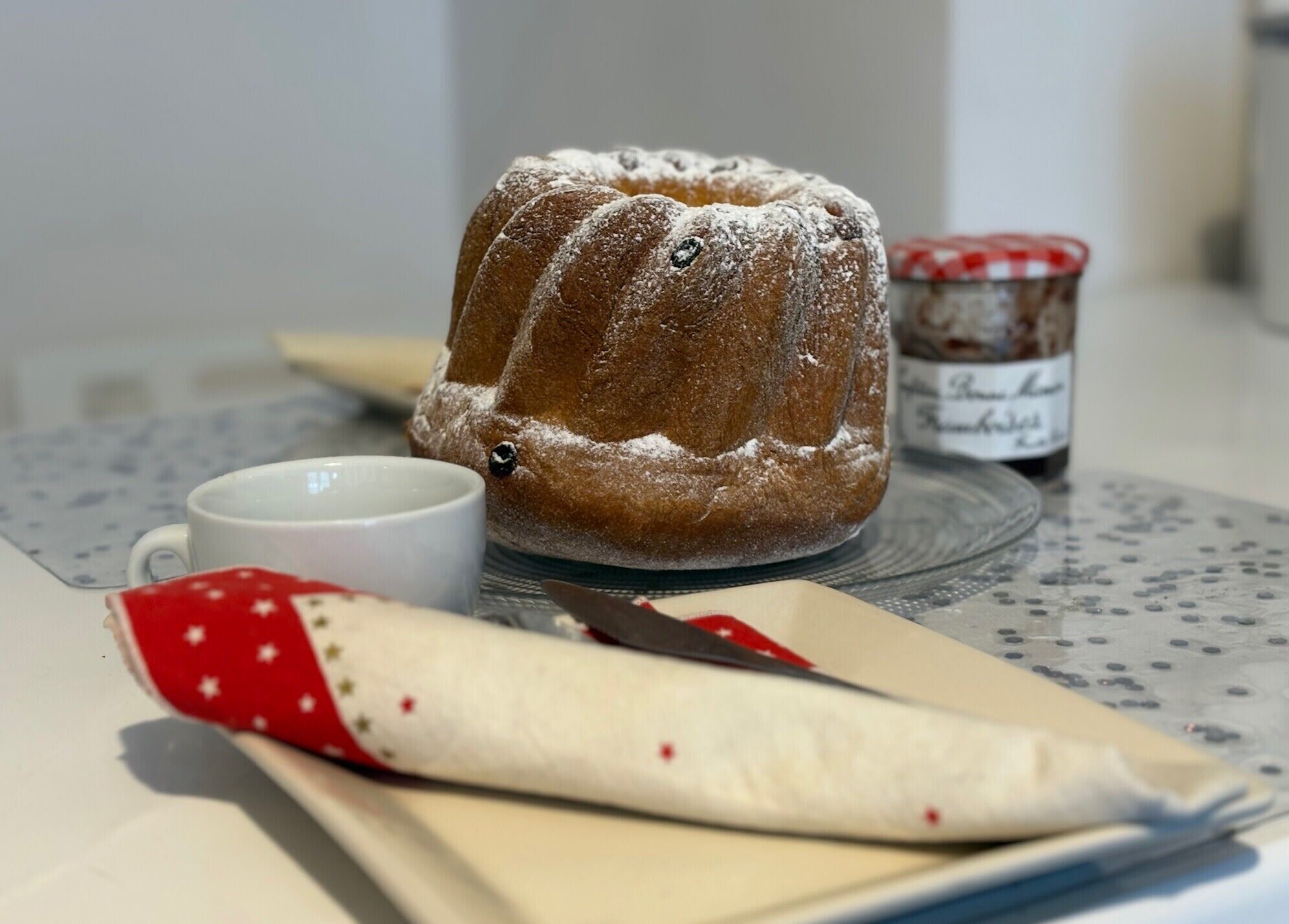 Een bundt cake op een bord, met een mes en een mok op een tafel.