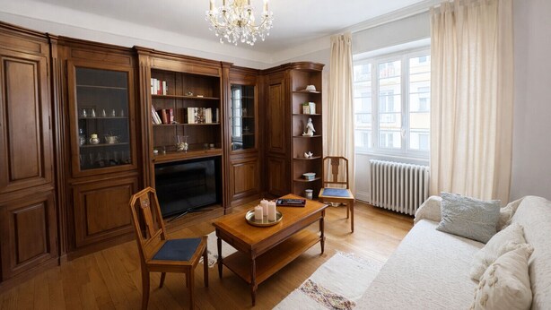 Un salon avec des meubles en bois, un lustre, une cheminée et une grande fenêtre avec des rideaux.