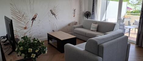 Un salón con un sofá gris, una mesa de centro, un televisor y una pared decorada con motivos de aves.