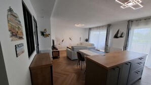 A modern kitchen with a central island, a dining area with a table and chairs, and a living area with a sofa and a TV.