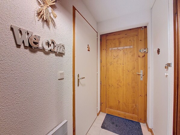 Um corredor com porta de madeira, uma placa de 'Welcome' e parede texturizada.