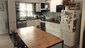 A modern kitchen with white cabinets, a wooden dining table, and a refrigerator covered in magnets and photos.