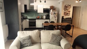 A modern living room with a sofa and chairs, a dining table, and a kitchen in the background.
