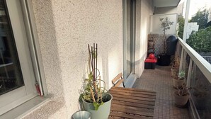 A balcony with a wooden bench, a potted plant, and a metal bucket.