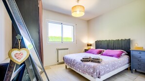 A bedroom with a bed, bedside tables, a window, a radiator, and a hanging heart-shaped decoration.