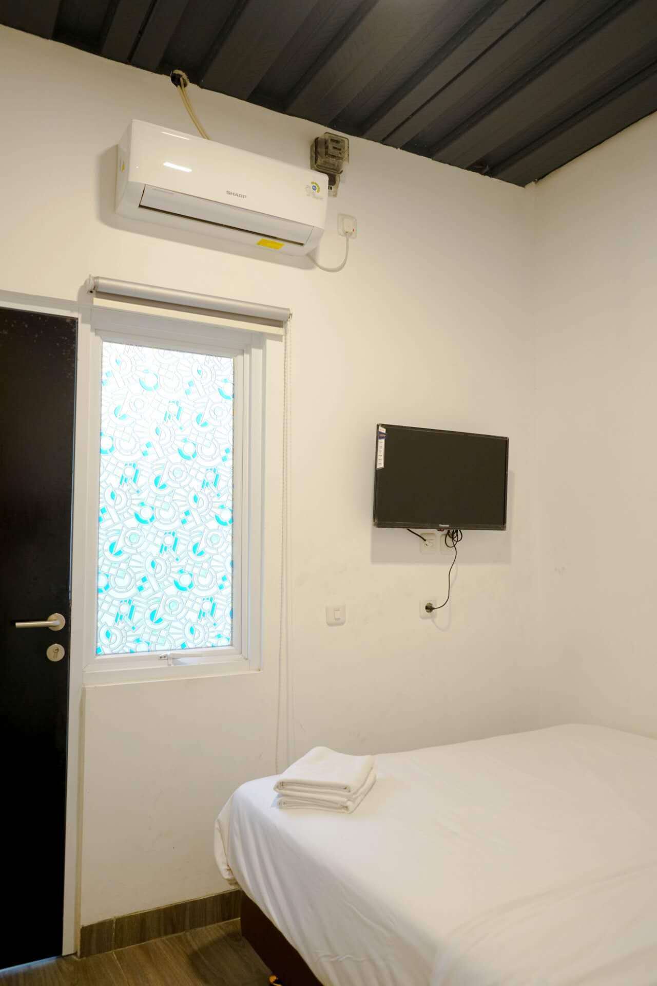 Quarto com uma cama, ar-condicionado, TV fixada na parede e uma porta com janela decorada.