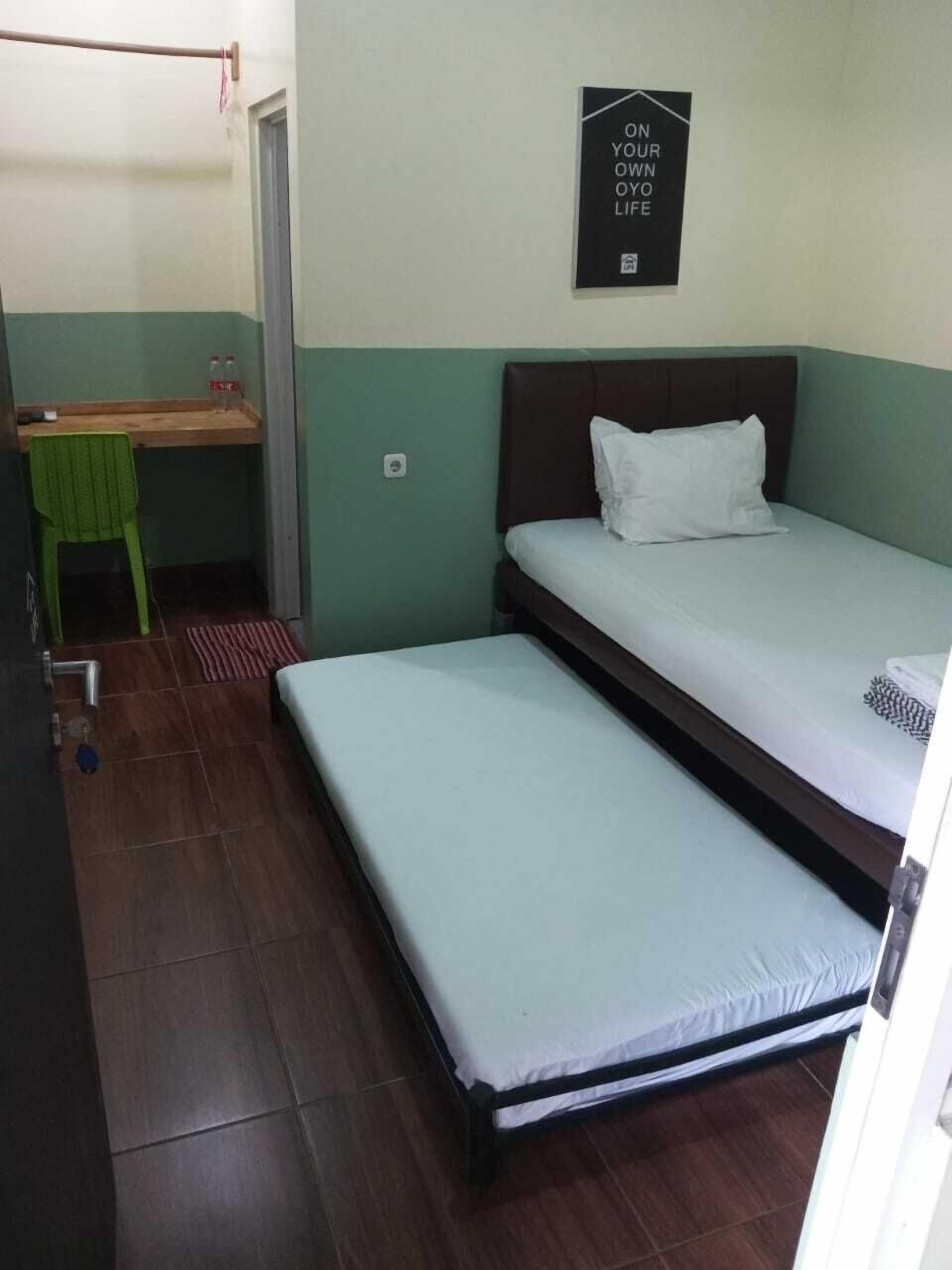 Una habitación pequeña y funcional con dos camas individuales, un escritorio y una silla.