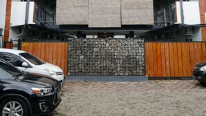 A modern building with a symmetrical facade, featuring a central entrance with a stone wall and a metal gate. - Puspiptek Residence Syariah (South Tangerang)