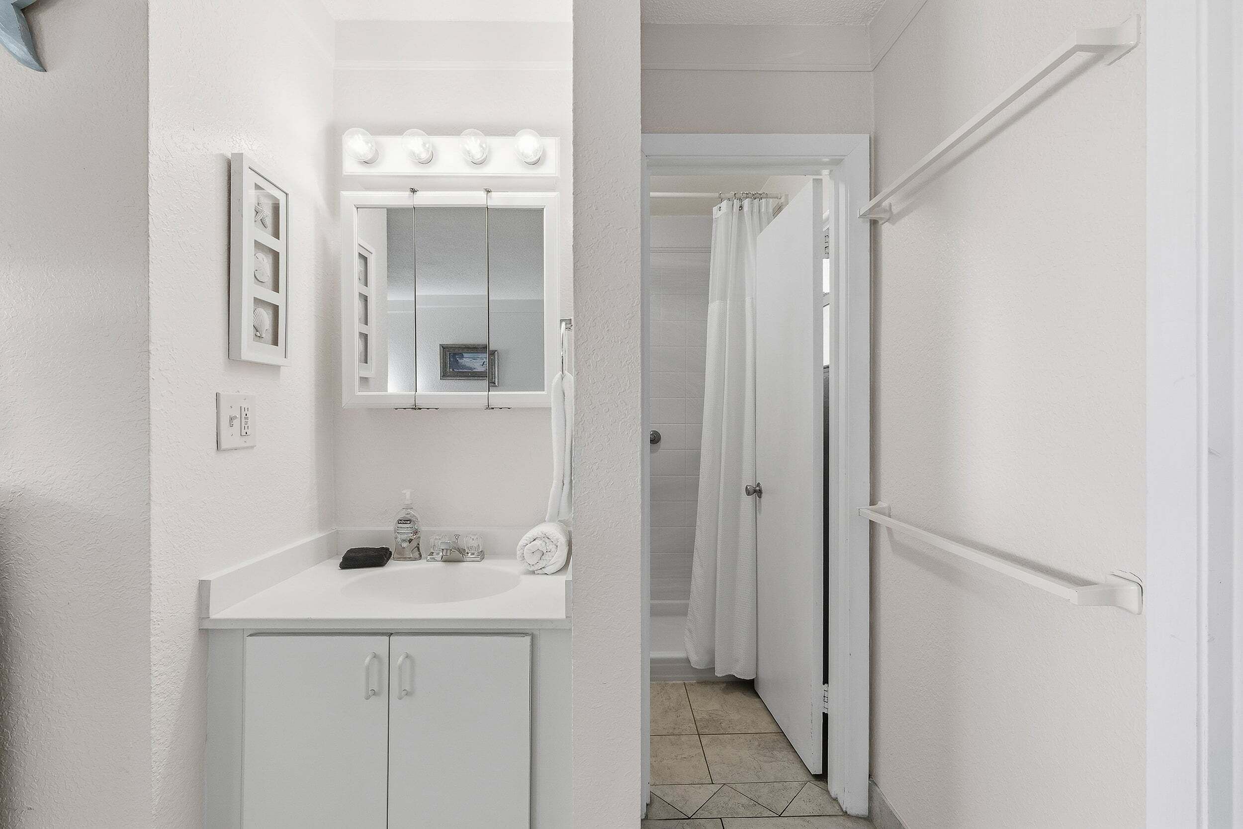 Une salle de bain avec un meuble-lavabo, un miroir avec éclairage intégré, un rideau de douche et une porte.