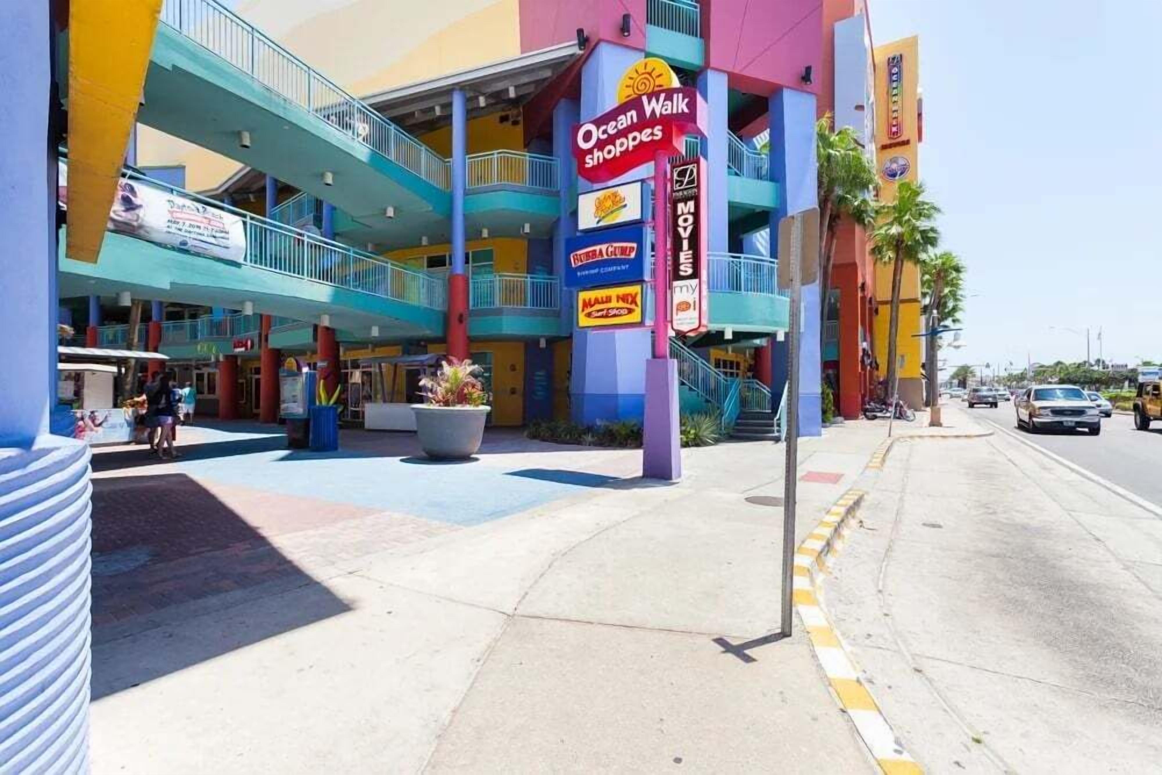 Un edifici de diversos pisos amb una façana colorida, destacant un cartell important per a Ocean Walk Shoppers.