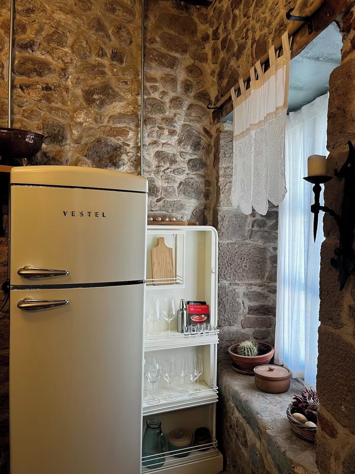 A vintage VESTEL refrigerator in a rustic stone-walled kitchen with a built-in wine rack, potted plants, and a candle holder.