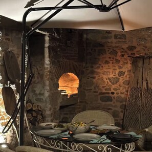 A rustic stone interior with a dining table set for a meal, surrounded by stone walls and a hanging light fixture. - A historic stone house, Ideal for visitors to the Acropolis-Asklepion in Bergama (İzmir)