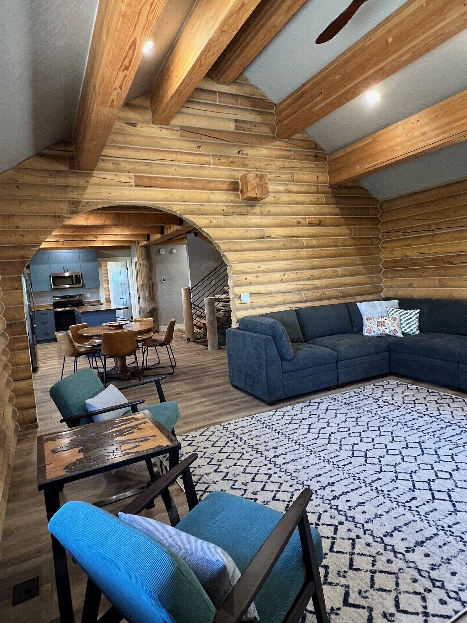 Un intérieur chaleureux avec des murs en bois, un coin repas comprenant des chaises et une table, un canapé et un tapis à motifs.