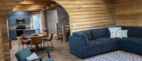 Un intérieur chaleureux avec des murs en bois, un coin repas comprenant des chaises et une table, un canapé et un tapis à motifs.