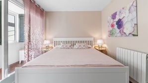 A bedroom with a bed, bedside lamps, a window with curtains, a radiator, and a floral wall art piece. - Holiday Home 'Deti' with Private Terrace and Wi-Fi (Roses)
