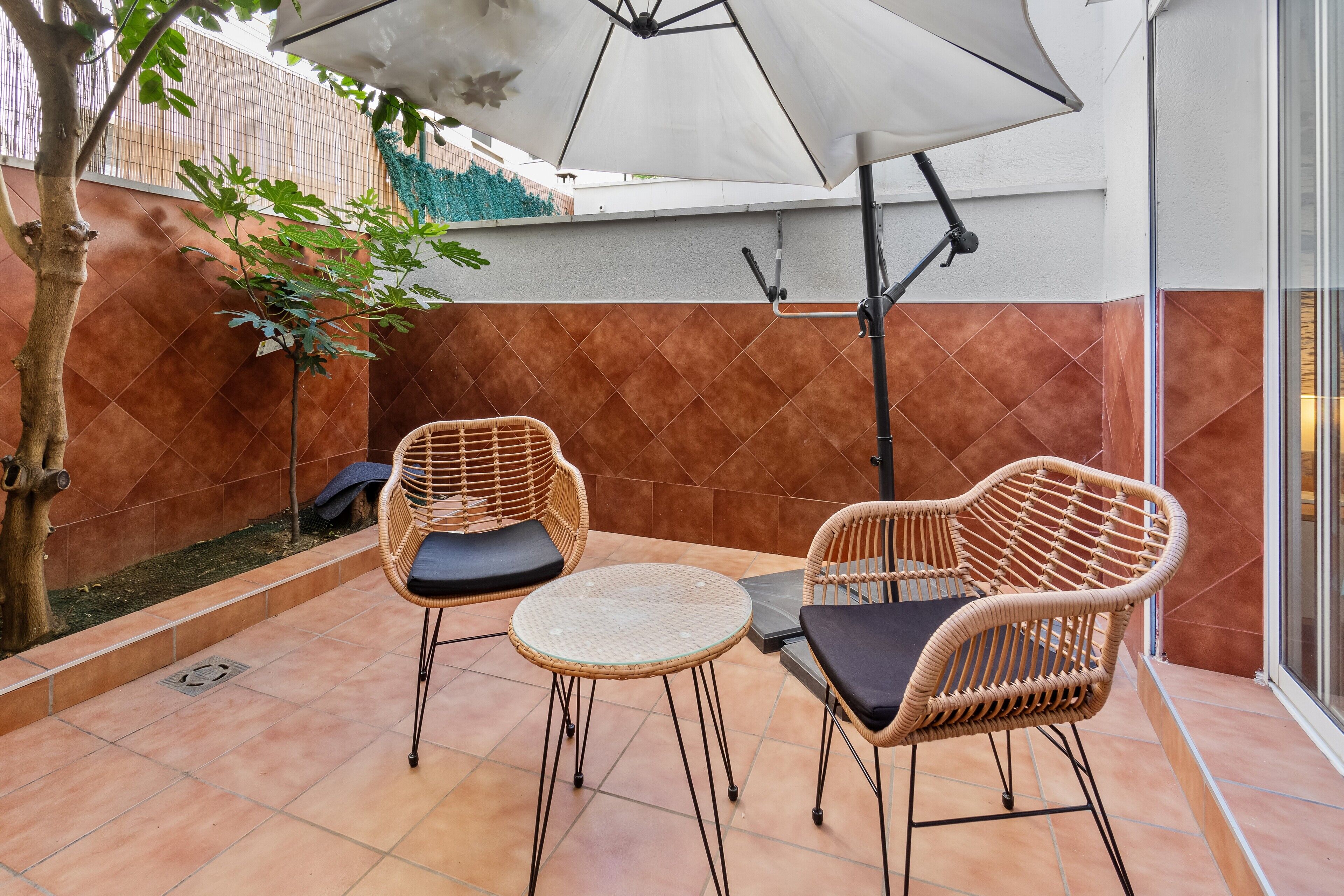 A patio with two wicker chairs, a small round table, and a white umbrella.