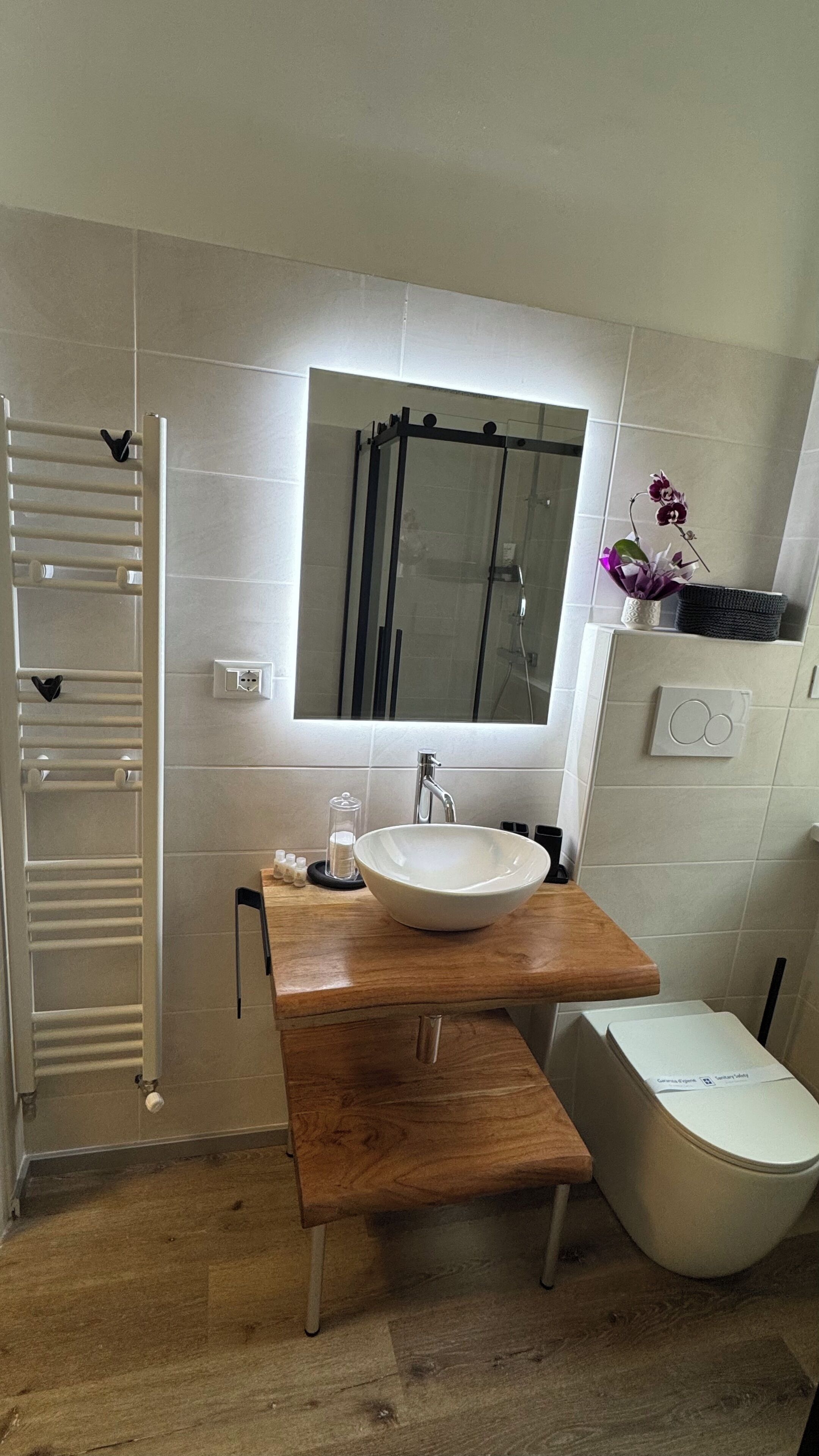 Un baño moderno con tocador de madera, lavamanos blanco, espejo y ducha.