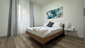 Une chambre à coucher moderne avec un lit en bois, du linge de lit blanc, un oreiller gris et une table de chevet fixée au mur.